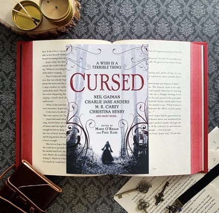 Copy of Cursed, edited by Marie O'Regan and Paul Kane, on the interior pages of a book with red sprayed edges on a dark wallpapered background