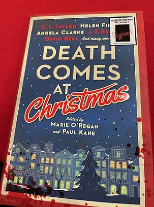 photograph of a copy of Death Comes at Christmas, edited by Marie O'Regan and Paul Kane, on a red tablecloth. Book features a SIGNED sticker