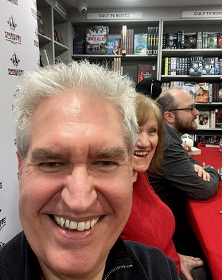 photo of a smiling Paul Kane. Behind him is a smiling Marie O'Regan, with Tom Mead in the background