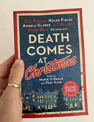 photograph of a man's hand holding up a proof copy of Death Comes at Christmas, edited by Marie O'Regan and Paul Kane