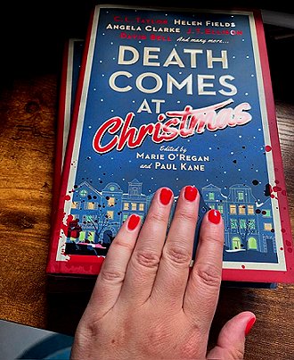 photograph of a woman's hand, with red-painted nails, on top of two copies of Death Comes at Christmas, edited by Marie O'Regan and Paul Kane, lying on a wooden surface