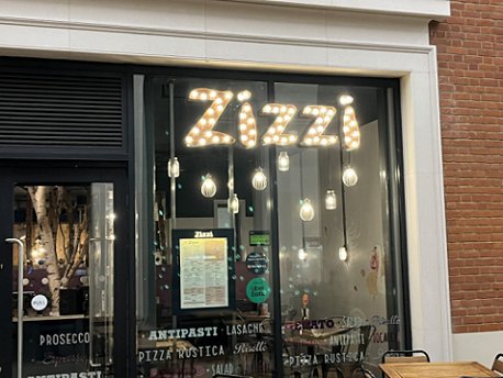 Exterior of a Zizzi's restaurant, showing the spotlit sign in a large glass window
