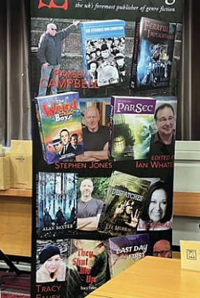 photograph showing the PS Publishing banner at Fantasycon. Books featured include 2023 Absinthe Books titles Despatches by Lee Murray, The Leaves Forget by Alan Baxter and They Shut Me Up by Tracy Fahey