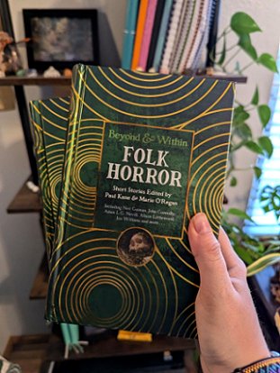 photograph of a woman's hand holding two copies of Beyond and Within Folk Horror, edited by Paul Kane and Marie O'Regan