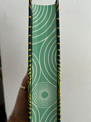 photograph showing the sprayed edges to the pages of Beyond and Within Folk Horror, edited by Paul Kane and Marie O'Regan. Page edges are sprayed green, with a repeating pattern of concentric gold circles