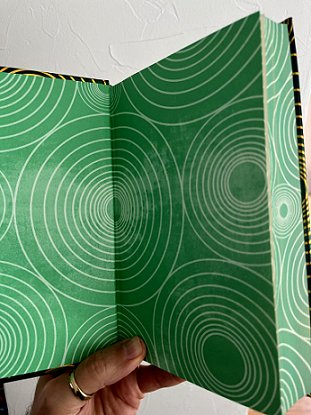 photograph showing the endpapers of Beyond and Within Folk Horror, edited by Paul Kane and Marie O'Regan. Pages are green, with a repeating pattern of gold concentric circles