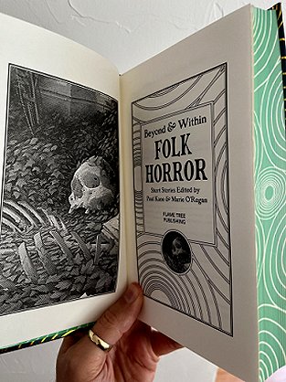 photograph of a man's hand holding up a copy of Beyond and Within Folk Horror, edited by Paul Kane and Marie O'Regan, to show the title page, which has the same pattern of concentric circles, and the black and white frontispiece illustration of a skeleton lying on a bed of leaves