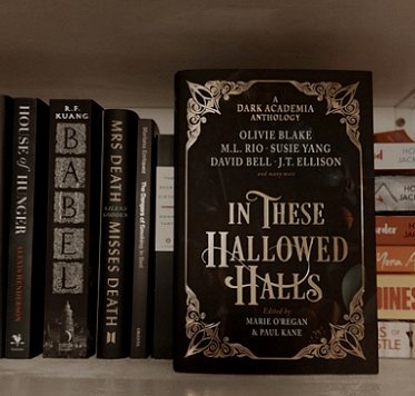 photograph of a hardback copy of In These Hallowed Halls, edited by Marie O'Regan and Paul Kane, standing in front of books on a shelf, including Babel by R.F. Kuang