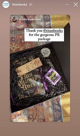screenshot showing a black box lined with purple and black tissue paper, containing a tied copy of In These Hallowed Halls, edited by Marie O'Regan and Paul Kane, as well as an Earl Grey teabag and In These Hallowed Halls candle