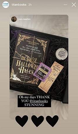 screenshot showing a black box lined with purple and black tissue paper, containing a tied copy of In These Hallowed Halls, edited by Marie O'Regan and Paul Kane, as well as a bookmark, an Earl Grey teabag and an In These Hallowed Halls candle