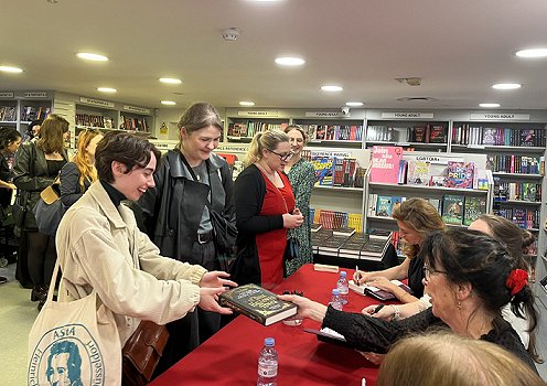 Queue of people waiting to have their copy of In These Hallowed Halls signed. Behind the table you can see Helen Grant and, behind her, Kate Weinberg