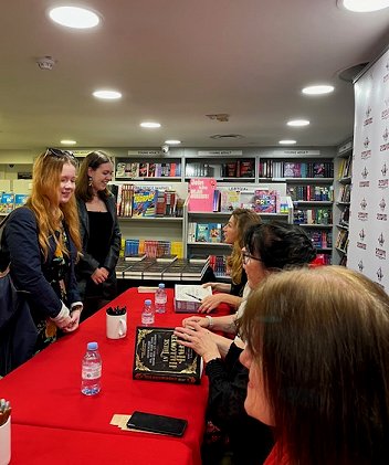 Two women having their copies of In These Hallowed Halls signed. In the foreground behind the table is Marie O'Regan. Behind her you can see Helen Grant and Kate Weinberg