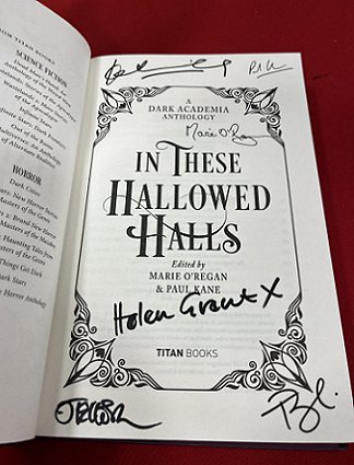 photograph of an open copy of In These Hallowed Halls, edited by Marie O'Regan and Paul Kane. The book is open to the title page, which has been signed by JT Ellison, Tori Bovalino, Helen Grant, Marie O'Regan, Kate Weinberg and Paul Kane