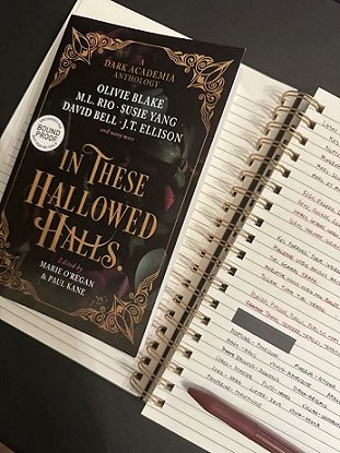 image showing a proof copy of In These Hallowed Halls, edited by Marie O'Regan and Paul Kane, lying on top of a spiral bound notebook filled with notes, with a red pen lying on top of those