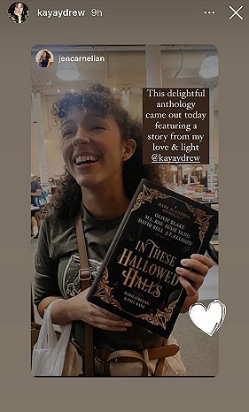 screenshot from @kayaydrew. A smiling woman holds up a copy of In These Hallowed Halls, edited by Marie O'Regan and Paul Kane. Text reads This delightful anthology came out today featuring a story from my love and light @kayaydrew