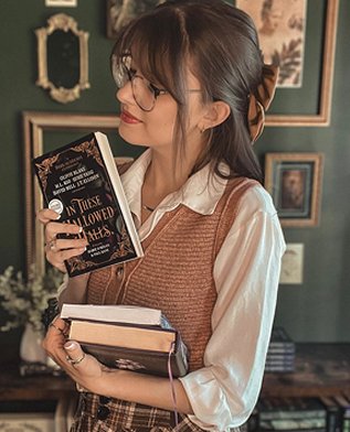 photograph showing Kelly Andrew holding two hardback books in one hand, and in the other she's holding up a proof copy of In These Hallowed Halls, edited by Marie O'Regan and Paul Kane