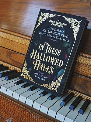 photograph of a copy of In These Hallowed Halls, edited by Marie O'Regan and Paul Kane, standing on the keys of a dark wood piano