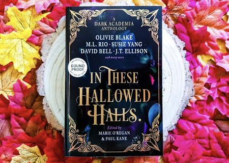 photograph showing a proof copy of In These Hallowed Halls, edited by Marie O'Regan and Paul Kane, lying on a white circle above pink orange and yellow leaves