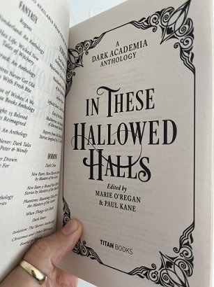 photograph of a man's hand holding up an open copy of In These Hallowed Halls, edited by Marie O'Regan and Paul Kane, to show the title page