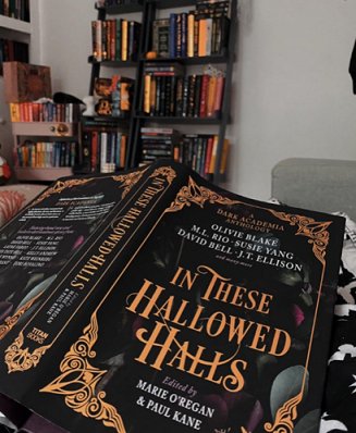 Image of a copy of In These Hallowed Halls, edited by Marie O'Regan and Paul Kane, lying facedown. Bookshelves in the background