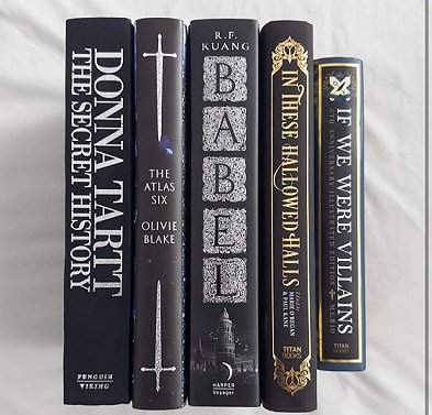 five books on a white background. The Secret History by Donna Tartt, The Atlas Six by Olivie Blake, Babel by R.F. Kuange, If We Were Villains by M L Rio, and In These Hallowed Halls, edited by Marie O'Regan and Paul Kane