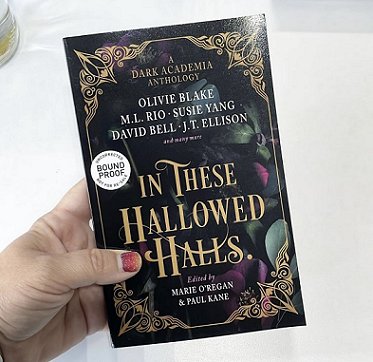 A woman's hand holding a copy of In These Hallowed Halls, edited by Marie O'Regan and Paul Kane, against a white background