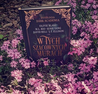 photograph of a copy of the Polish edition of In These Hallowed Halls, edited by Marie O'Regan and Paul Kane, standing in the middle of a group of pink flowers