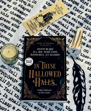 A copy of In These Hallowed Halls, edited by Marie O'Regan and Paul Kane, lying on a lettered cloth, with a candle and bookmark beside it