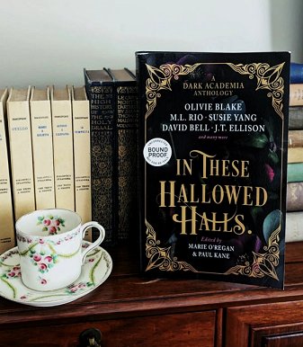 Bookshelf, with a teacup and saucer beside a standing copy of In These Hallowed Halls, edited by Marie O'Regan and Paul Kane