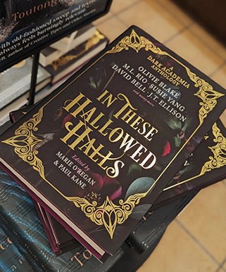 image of a copy of In These Hallowed Halls, edited by Marie O'Regan and Paul Kane, lying on top of a stack of books on a table