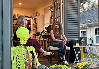 photograph of a woman interviewing M L Rio outside a bookstore. A yellow skeleton is in the foreground