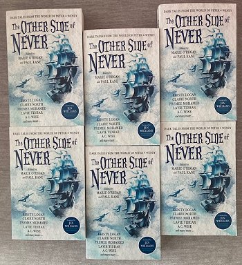Six copies of The Other Side of Never, edited by Marie O'Regan and Paul Kane, on a wooden table