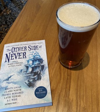 A copy of The Other Side of Never, edited by Marie O'Regan and Paul Kane, on a wooden table next to a pint glass of beer