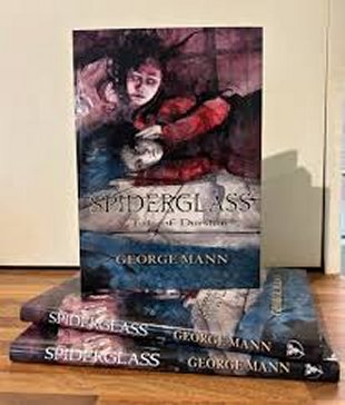 image showing a copy of Spiderglass: A Tale of Durstan by George mann, on top of two flat copies on a wooden surface