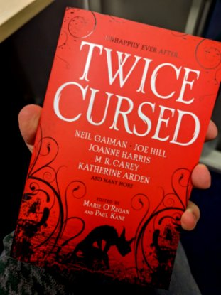 Image of a man's hand holding a copy of Twice Cursed, edited by Marie O'Regan and Paul Kane