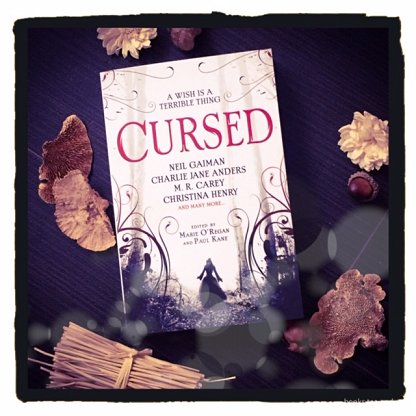 image of a copy of Cursed, edited by Marie O'Regan and Paul Kane, on a black background and surrounded by gold and brown leaves and twigs