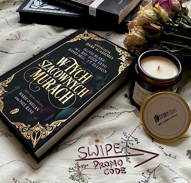 photograph of a copy of the Polish edition of In These Hallowed Halls, edited by Marie O'Regan and Paul Kane, on a cream cloth, beside a brown glass jar candle, dried flowers and two hardback books