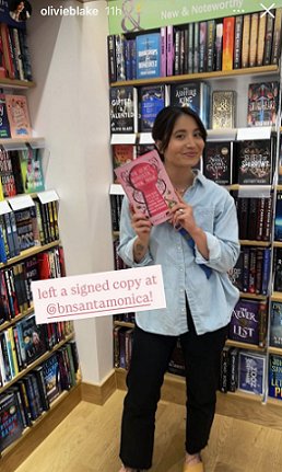 photograph of a smiling Olivie Blake holding up a copy of The Secret Romantic's Guide to Magic, edited by Marie O'Regan and Paul Kane. Text reads 'left a signed copy at @bnsantamonica!'
